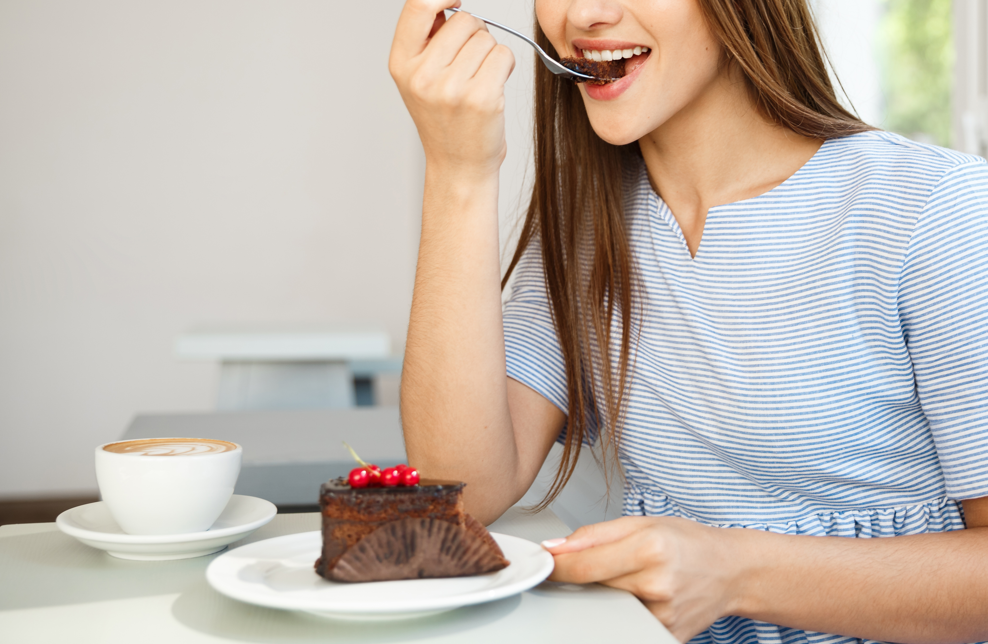 Young attractive Caucasian lady enjoy eating chocolate cake with hot coffee in modern coffee shop at noon.