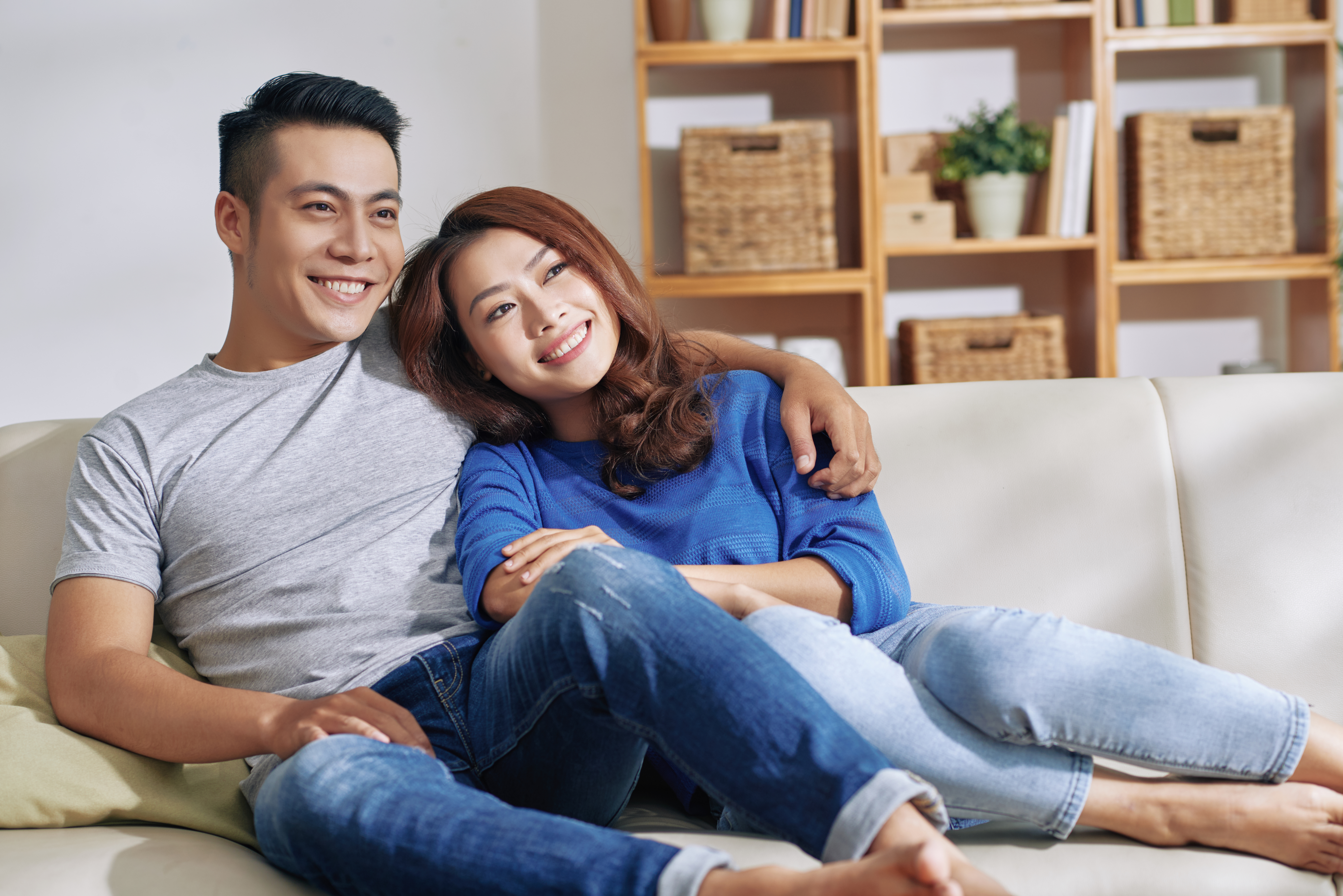 happy-asian-couple-sitting-couch-together-home-looking-away-smiling
